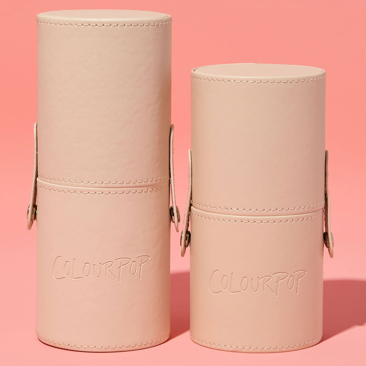 ColourPop Small Stash Cup standing upright - two nude, faux-leather cylindrical holders with snap side straps, stitched trim, and embossed logo - organizing makeup tools and accessories, shown side by side on a pink backdrop.