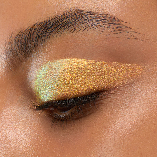 ColourPop Chrome Liquid Shadow in Glaze sweeping across a closed eyelid in a smooth, winged application, shifting gold to mint-green with high-shine shimmer; close-up shows opaque, multidimensional chrome payoff.