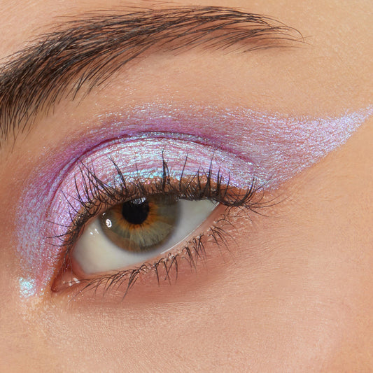 Close-up eye wearing Colourpop Disco Disco Shadow Stix, showing iridescent pink-lavender cream eyeshadow swept across the lid and extended into a sharp wing for a bold, shimmering makeup look.