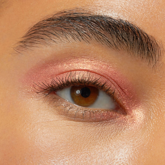 Brown eye wearing Friday Feels Shadow Stix, a shimmering rose-gold pink from the ColourPop Shadow Stix line, swept across the lid and inner corner with a soft metallic sheen in a close-up beauty swatch.