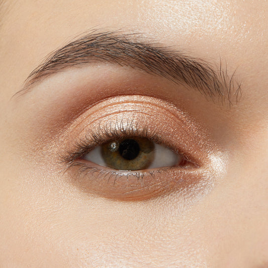 Eyelid wearing Honey BB ColourPop Shadow Stix, a warm honey‑gold shimmer cream eyeshadow, swept across the lid and inner corner for a glossy metallic glow, softly blended at the crease beneath a natural brow.