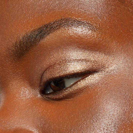 Shimmery champagne-bronze eyeshadow sweeps across a closed eyelid, showcasing the Walk of Fame shade from ColourPop Shadow Stix in a tight close-up beauty swatch under soft light.