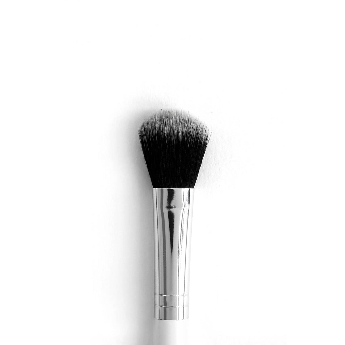 ColourPop Small Fluff Brush makeup brush blending and packing shadow, featuring dense black-to-gray fluffy bristles with a domed edge, a polished silver ferrule, and a white handle, shown upright on a clean white background.
