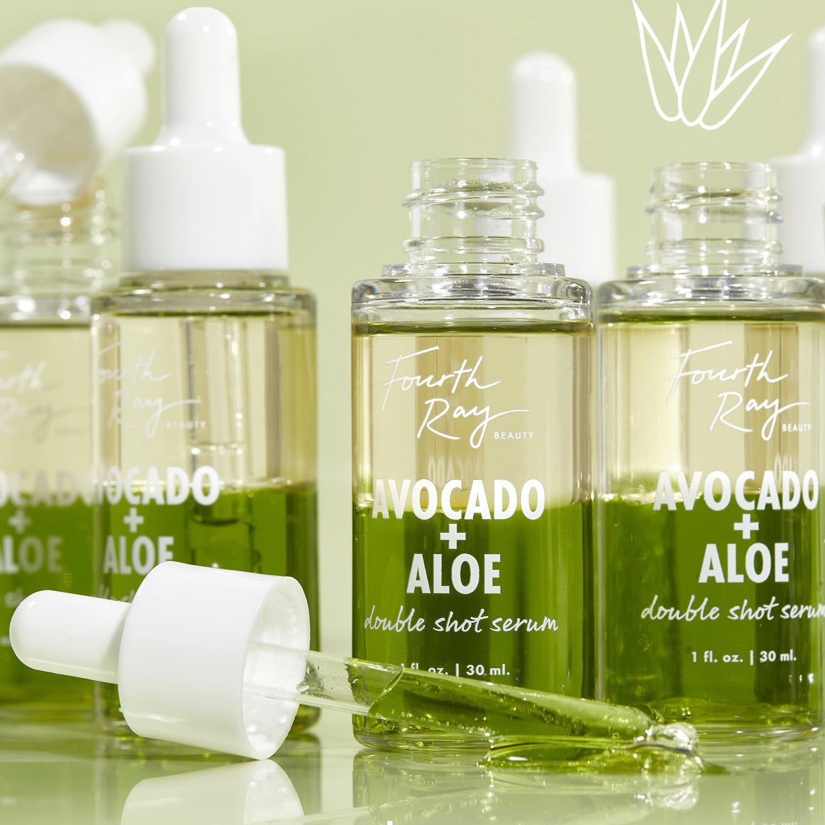 Fourth Ray Beauty Avocado + Aloe Double Shot, a ColourPop Face Serum, stands in clear 1 fl oz (30 ml) glass bottles as a dropper releases the vibrant green formula on a glossy surface against a pale green studio backdrop.