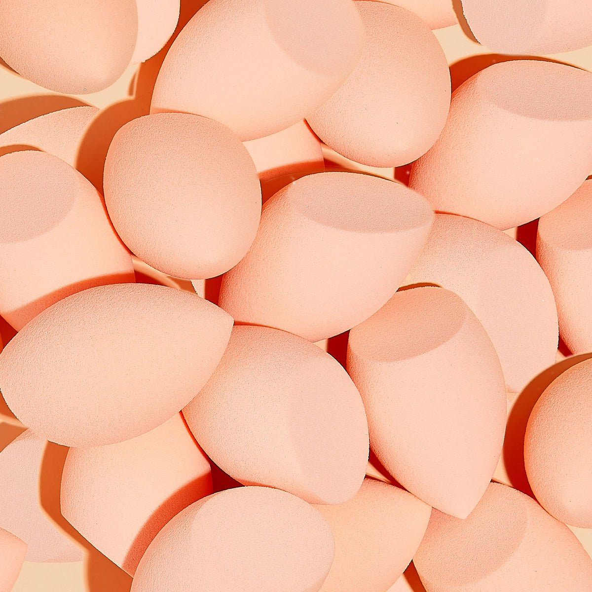 Blending Sponge set - peach, teardrop foam applicators - scattered in a close-up pile, showing rounded bases and pointed tips on a warm beige backdrop for seamless foundation and concealer blending; ColourPop Makeup Tools & Accessories.