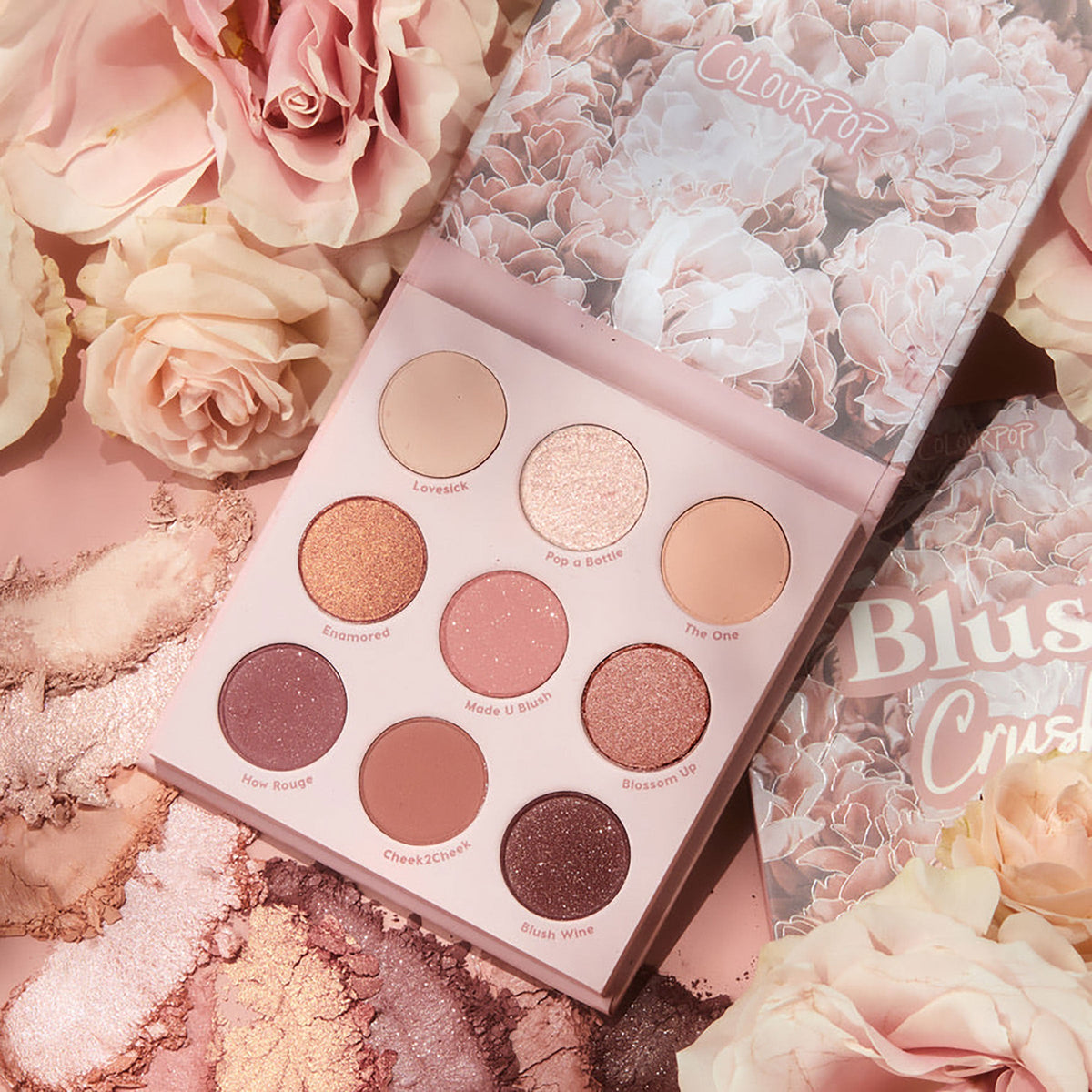 Blush Crush ColourPop Shadow Palette lying open to reveal nine rosy neutrals in matte and shimmer finishes, from champagne to deep plum, displayed with floral-printed lid, pink roses, and crushed shadow swatches on a blush backdrop.