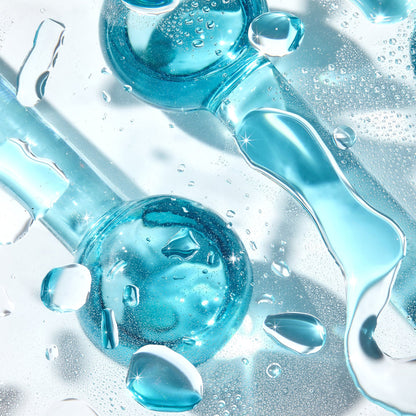 Cooling Facial Globes glisten as blue glass spheres with handles roll among water droplets on a clear surface, highlighting a chilled de-puffing facial massage tool set from ColourPop Skincare Tools And Accessories.
