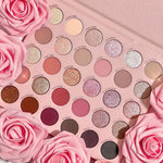 Smoke 'N Roses shadow palette by ColourPop lies open, displaying 30 rose-toned mattes, shimmers, and pressed glitters - from soft nude and mauve to deep charcoal and black - in a pink tray framed by pink roses; ColourPop Shadow Palette.