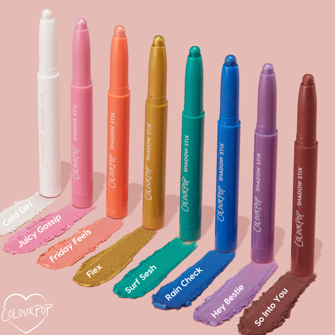 ColourPop Shadow Stix in Juicy Gossip - a shimmering bubblegum pink - shown with tip extended and a creamy swatch below, standing among other shades on a soft pink backdrop; twist-up eyeshadow crayon for quick, one-swipe color.