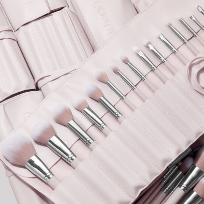 Stone Cold, a ColourPop Makeup Brush Kit, fanned in a blush-pink roll as face and eye brushes slot into stitched pockets, soft white-to-pink bristles and silver ferrules gleaming, with additional matching brush rolls layered behind.