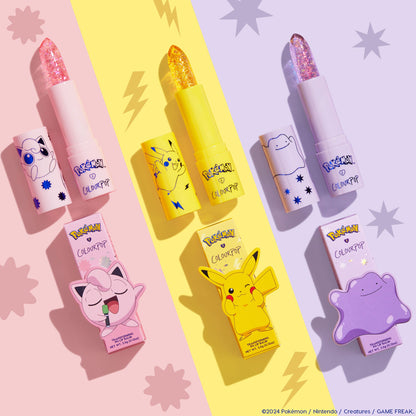 Sing pH Lip Balm by ColourPop x Pokémon, uncapped to show a pink glitter bullet with Jigglypuff art on a pastel pink tube, set in a flatlay alongside Pikachu and Ditto versions on a split pastel backdrop. ColourPop pH Lip Balm.