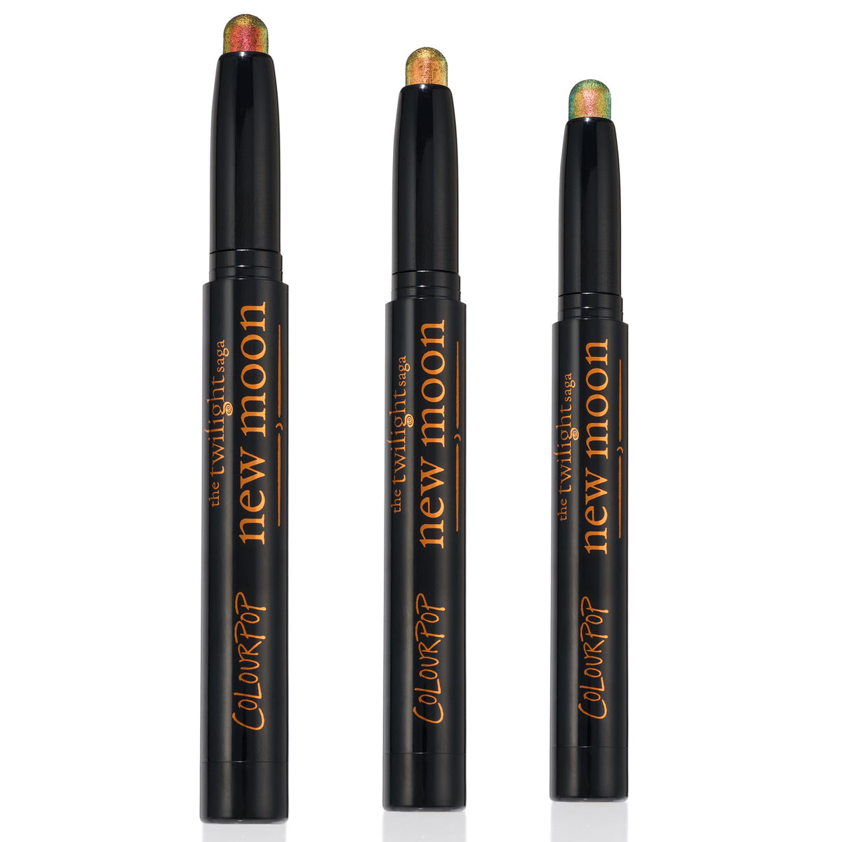 Love Triangle trio of ColourPop Shadow Stix stand uncapped to display shimmery multichrome tips - copper-red, golden bronze, and green-teal - in sleek black twist-up pens with The Twilight Saga New Moon branding, set against a clean white background.
