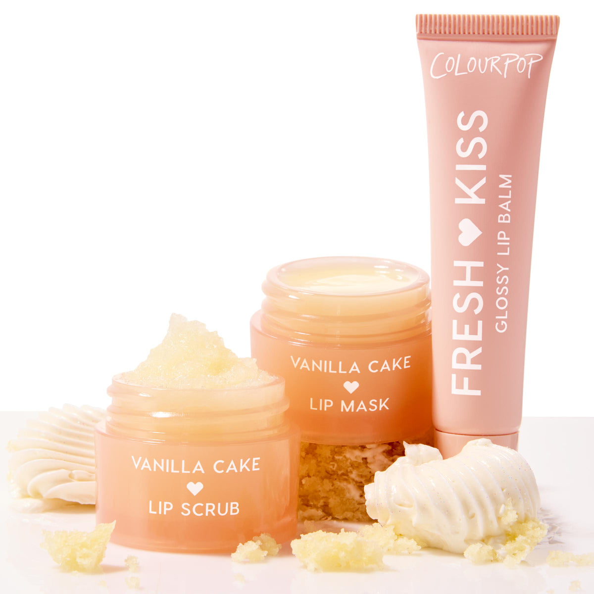 Vanilla Dream ColourPop Lip Care Kit featuring Vanilla Cake lip scrub, Vanilla Cake lip mask, and Fresh Kiss glossy lip balm, arranged on a white surface with cake crumbs and frosting swirls, peach-toned jars and creamy textures.