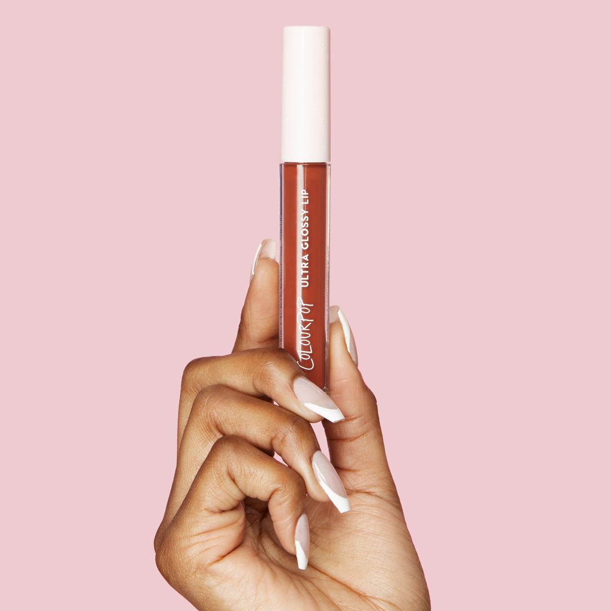 ColourPop Ultra Glossy Lip in Coffee Break held upright by a manicured hand, showcasing a clear tube with a white cap and warm coffee-brown gloss against a soft pink background.