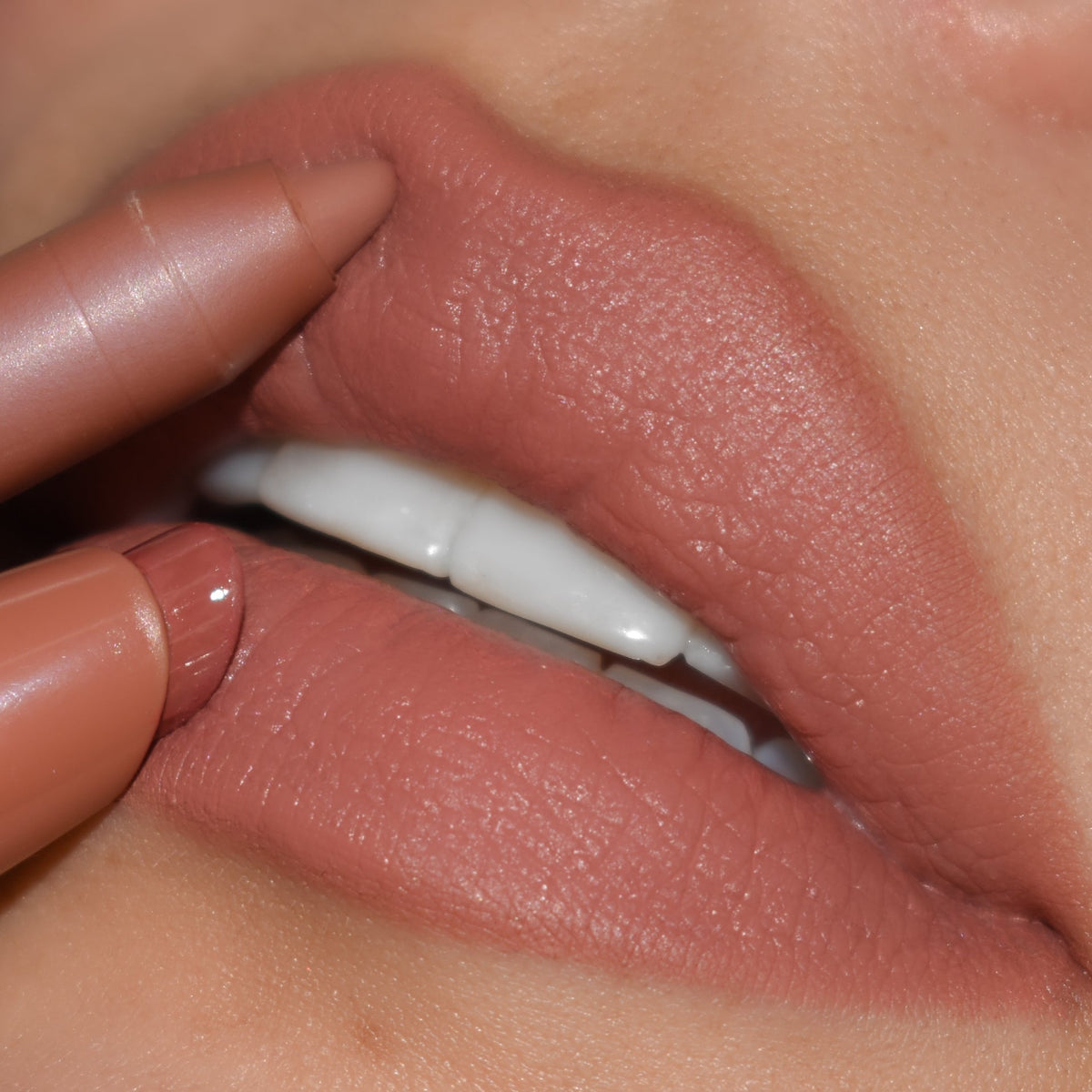 ColourPop Cookie Lippie Stix gliding onto lips, paired with a matching nude liner to define the cupid’s bow, showcasing a creamy warm beige-nude color in a tight close-up beauty shot.