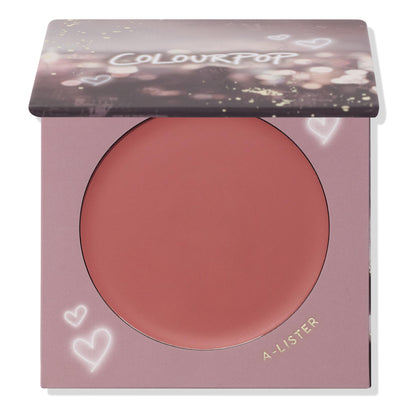 ColourPop Cream Blush A-Lister compact displaying a warm rosy-mauve pan, lid half-closed with bokeh print, set in lavender packaging with heart doodles and gold A-LISTER text, studio-lit on a white background.