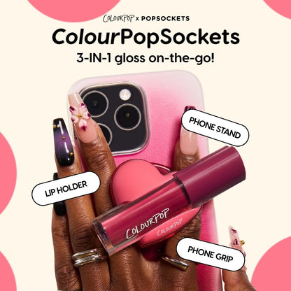 ColourPop Lip Stain tube snaps into a pink heart-shaped ColourPopSockets holder on a gradient pink smartphone, functioning as phone grip, stand, and lip holder while a hand with floral nail art grips the device - 3-in-1 on-the-go lip stain.
