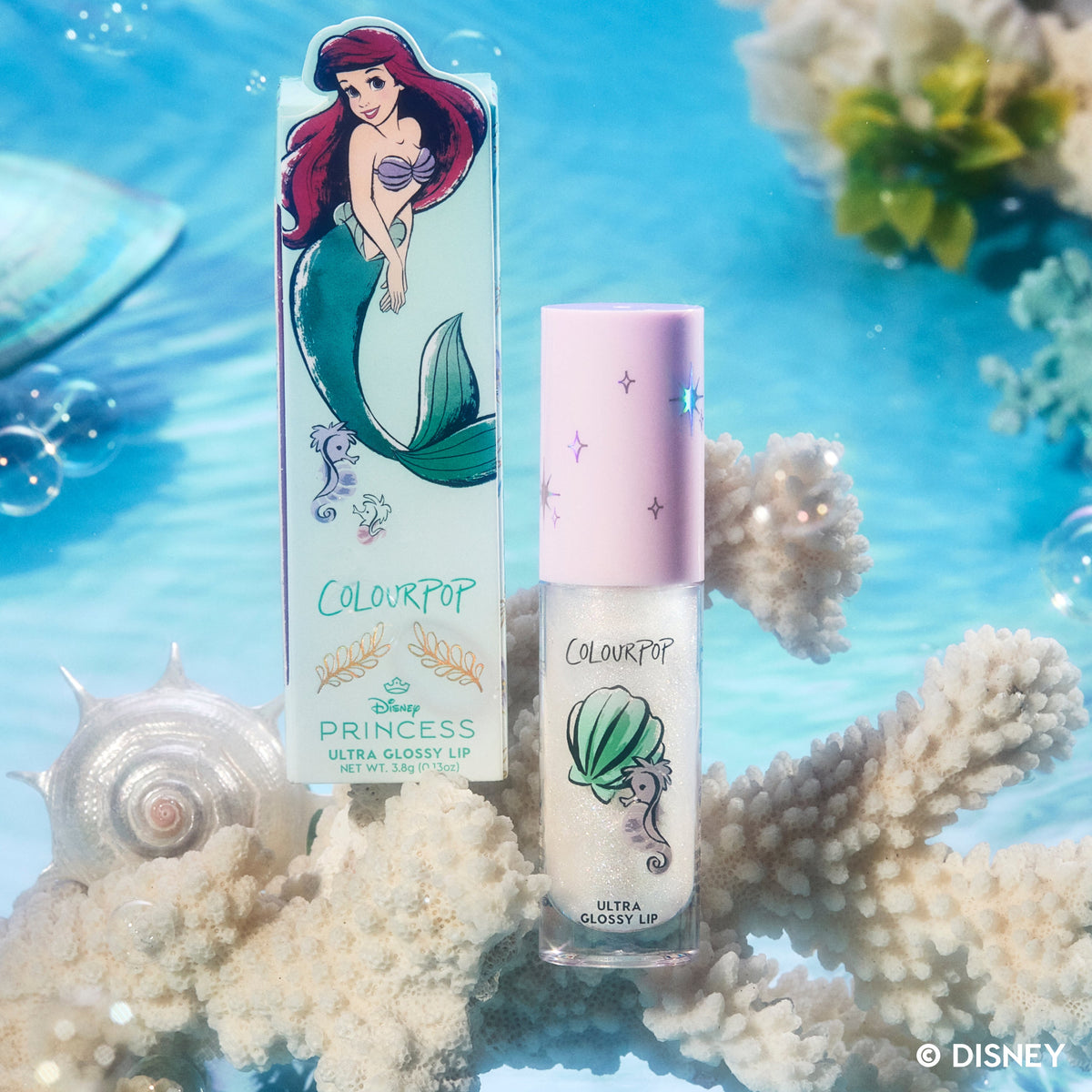 ColourPop Bright Ariel Ultra Glossy Lip from the Disney Princess collection standing on coral, with Ariel artwork on the mint box and shimmering gloss tube against an underwater-inspired blue background with bubbles and seashells.