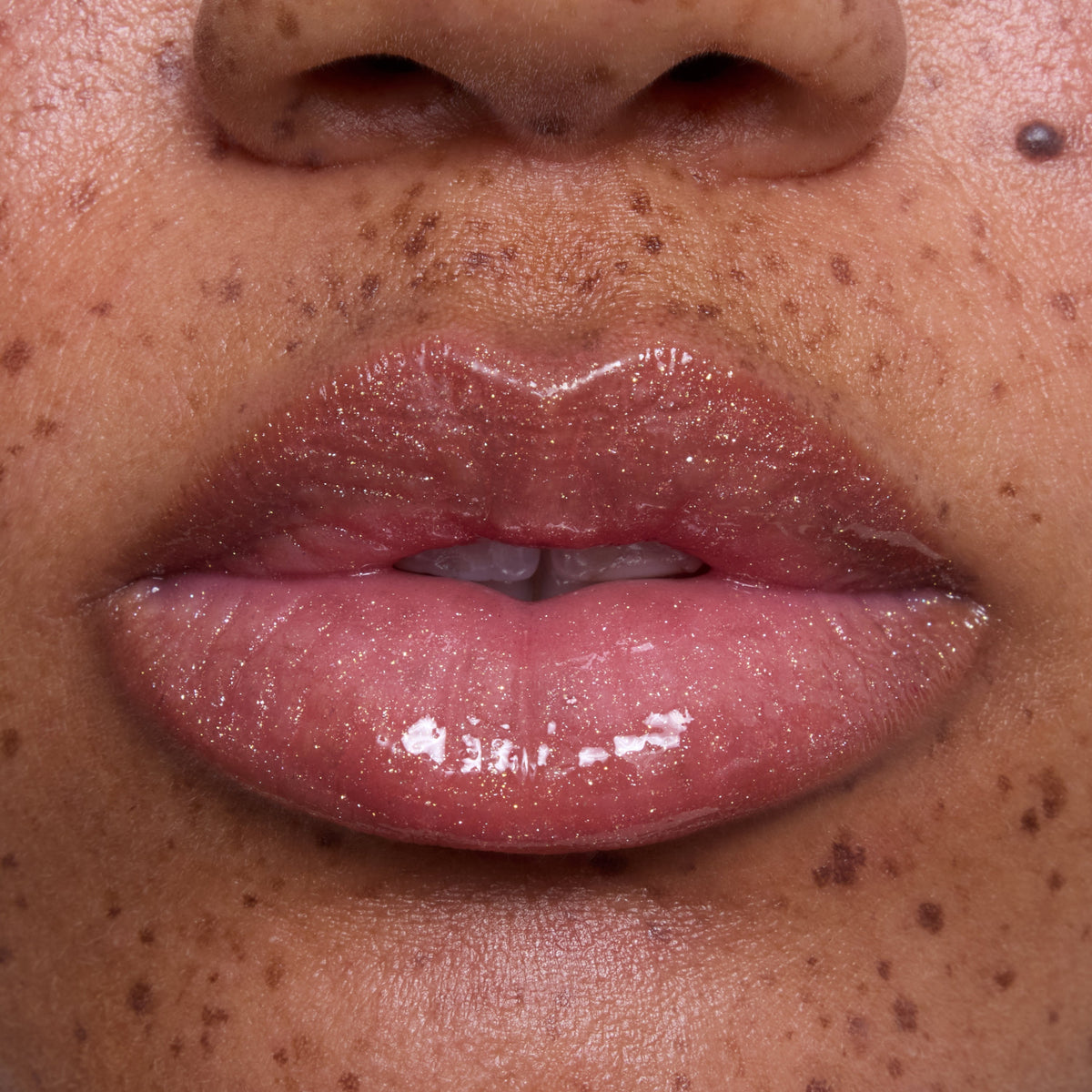 Close-up of freckled lips wearing Mademoiselle Belle Ultra Glossy Lip, a sheer pink Disney Princess lip gloss with high-shine, shimmery finish on medium skin tone, showcasing smooth, hydrated texture for beauty product detail.