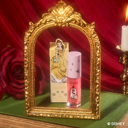 ColourPop Mademoiselle Belle Ultra Glossy Lip stands beside its yellow Disney Princess Belle box inside an ornate gold mirror frame, styled with a red rose, candle, and red velvet backdrop for a fairytale-inspired makeup product shot.