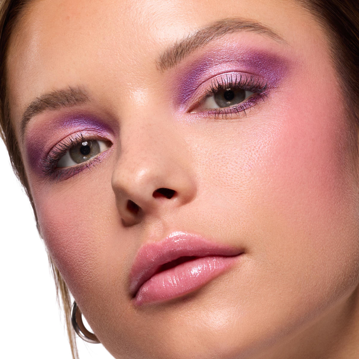 Violet and lilac shimmer blended across lids on a model, showcasing the ColourPop It’s My Pleasure shadow palette; close-up beauty shot with soft pink blush, defined lashes, and glossy pink lips on dewy skin.