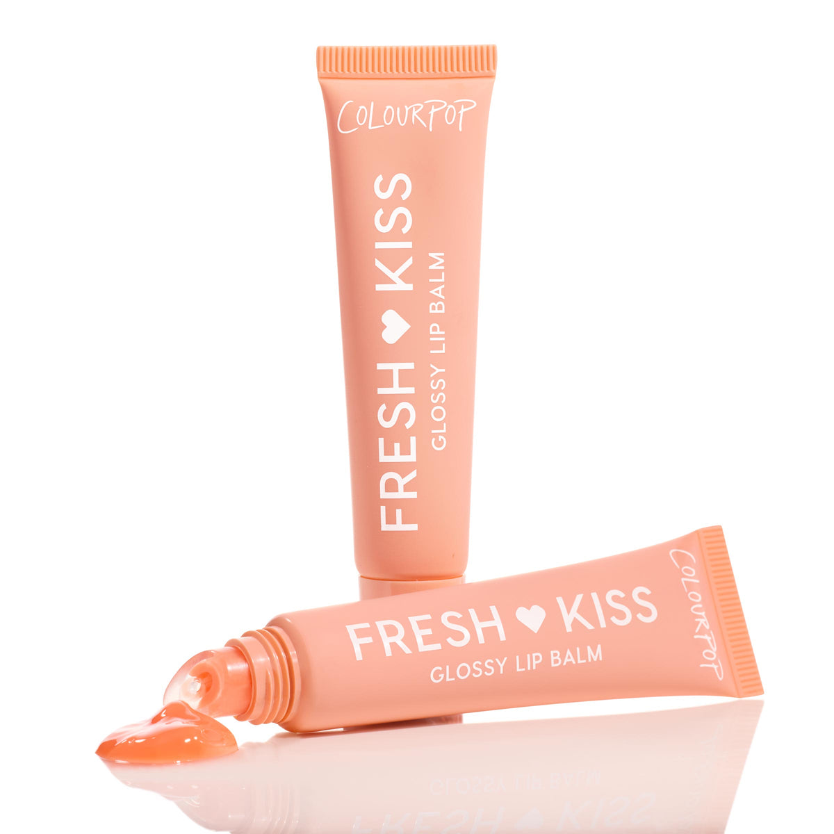 ColourPop Fresh Kiss Glossy Balm in Mango Sorbet, peach squeeze tube with white lettering, stands upright beside a second tube releasing a glossy peach gel onto a reflective white surface, highlighting the slanted applicator tip.