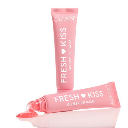 ColourPop Fresh Kiss Glossy Balm, Strawberry Milk shade - one pink tube upright and another squeezed with a rosy gloss bead at the slanted tip, shown on a reflective white surface in a clean studio close-up.