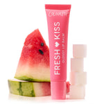 ColourPop Fresh Kiss Glossy Balm in Watermelon Sugar stands upright in a pink squeeze tube, flanked by a seeded watermelon wedge and stacked sugar cubes on a white studio surface, highlighting the fruity, glossy lip balm.
