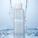 Fourth Ray Beauty Waterfall Gentle Tonic face toner standing upright as water splashes around it, showcasing a pale blue 4.15 fl oz bottle with white flip cap; hydrating ColourPop Face Toner in a fresh waterfall setting.