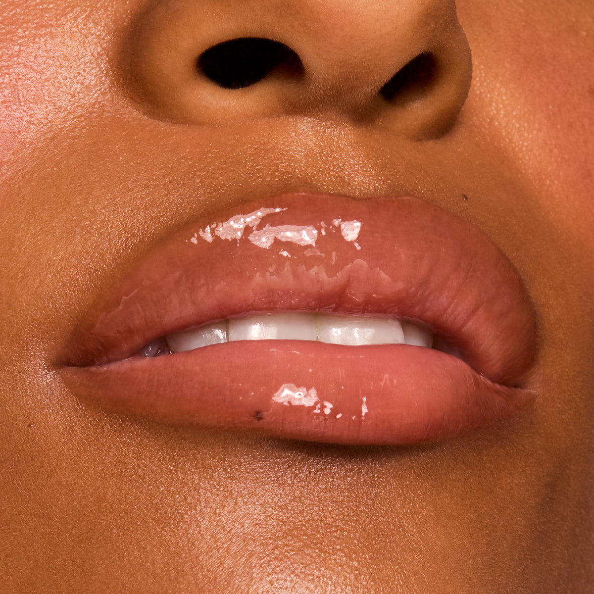 Glossy lips wearing ColourPop Fresh Kiss Glossy Balm in Caramel Latte, showing a high-shine, sheer caramel nude tint on a close-up mouth with teeth slightly visible in a tight macro beauty shot.
