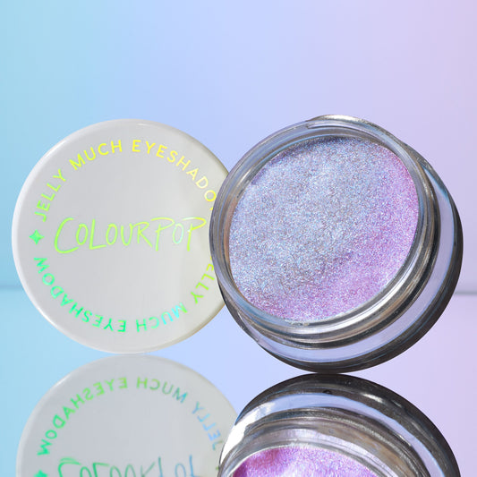 ColourPop Jelly Much Shadow Hallucinogenius opens to reveal an iridescent lavender-blue jelly eyeshadow with metallic shimmer, its white lid with COLOURPOP logo beside it, mirrored on a glossy surface against a pastel blue-purple backdrop.