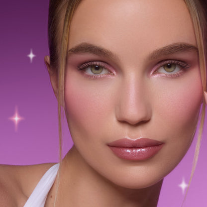 Model wearing Heart to Get All Eyes On Me Shadow Stix Set, showing shimmering pink eye shadow and soft blush on flawless skin against a glowing purple background with star accents, highlighting the eye makeup look for US beauty shoppers.