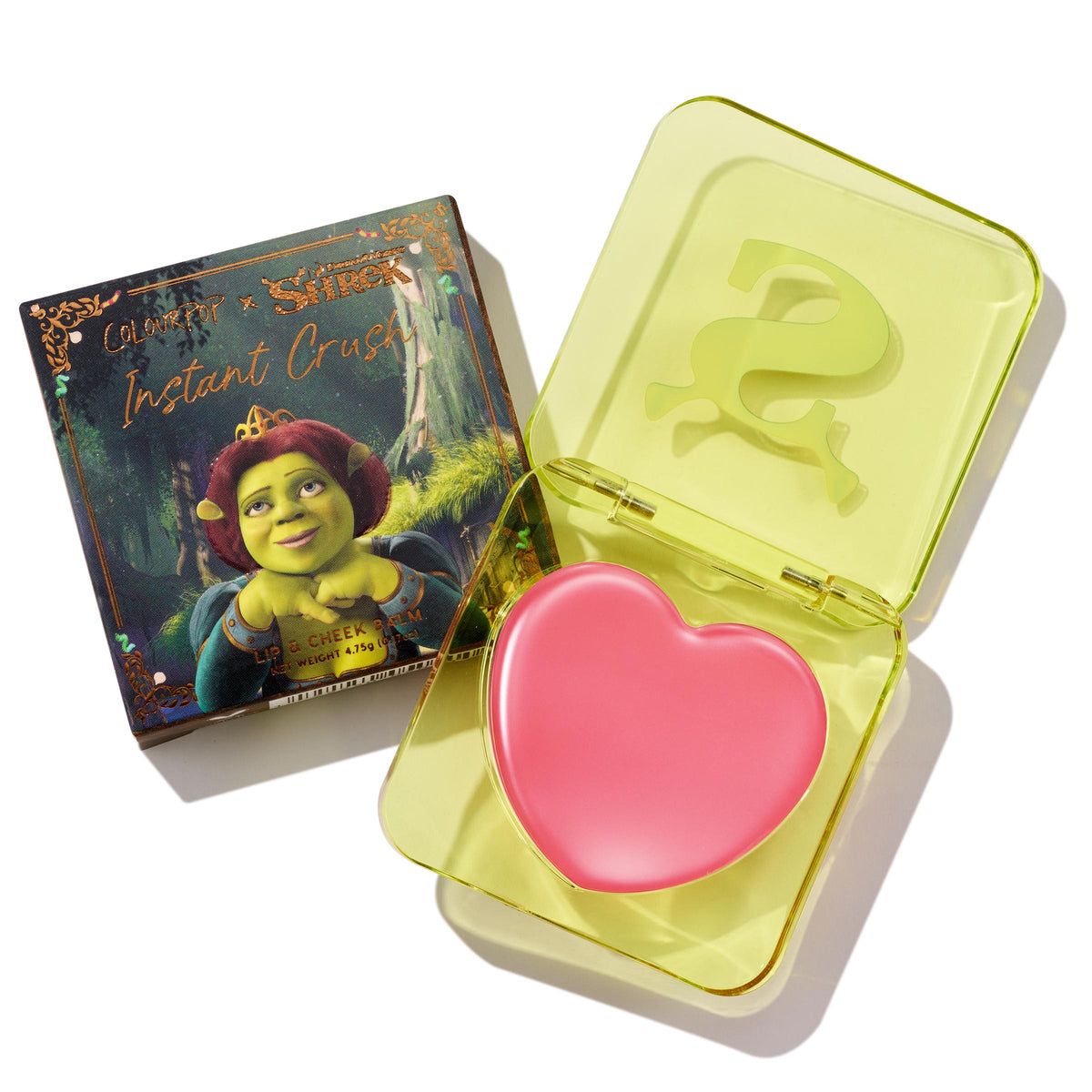 Heart-shaped pink True Love’s Form ColourPop Lip and Cheek Balm sits open in a translucent neon-yellow compact with an embossed S logo, placed beside its ColourPop x Shrek box featuring Princess Fiona artwork.
