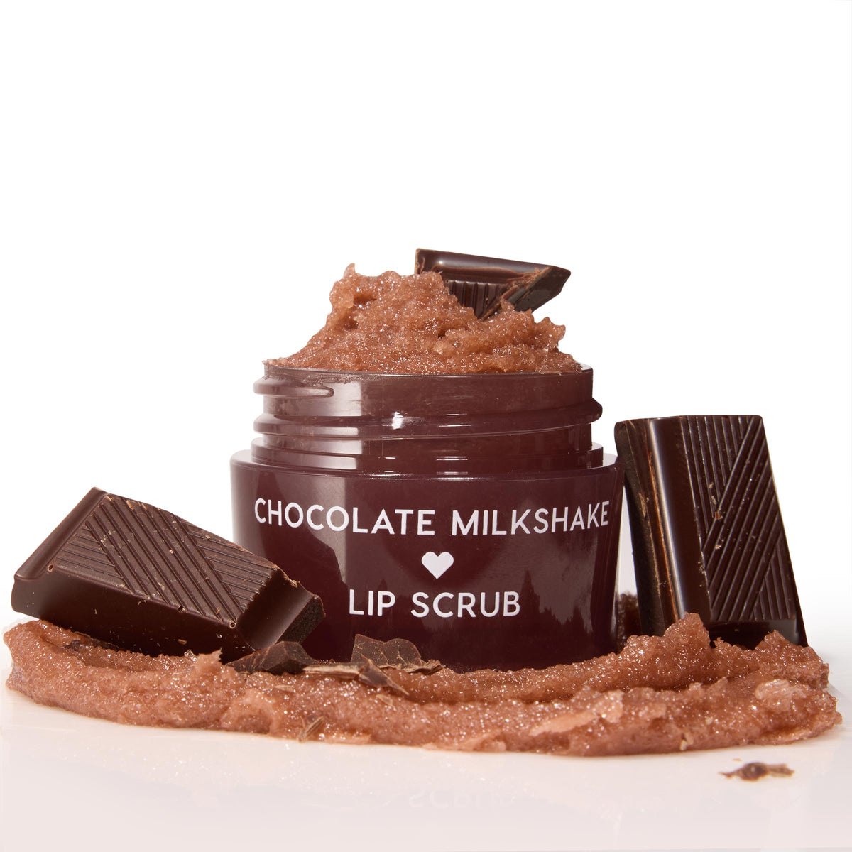 Chocolate Milkshake ColourPop Lip Scrub mounded in an open maroon jar, with the sugary brown exfoliant swatched in a thick smear and framed by dark chocolate bar pieces on a white studio backdrop.