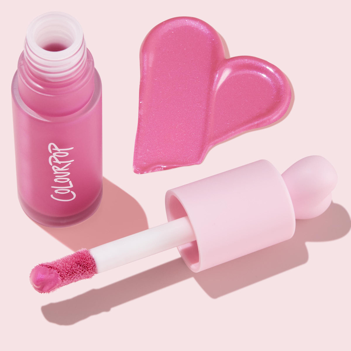ColourPop Liquid Blush Sweet Treat shown with frosted pink bottle and doe-foot applicator, product swatched in a glossy heart, bright bubblegum pink with subtle shimmer, set on a soft pastel pink background.