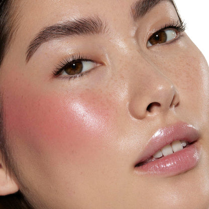 Cheeks glow with dewy rosy pink I Love It by ColourPop Liquid Blush, blending seamlessly to a luminous sheen on a close-up face with natural freckles, brown eyes, and glossy lips, showcasing smooth, buildable color in studio lighting.