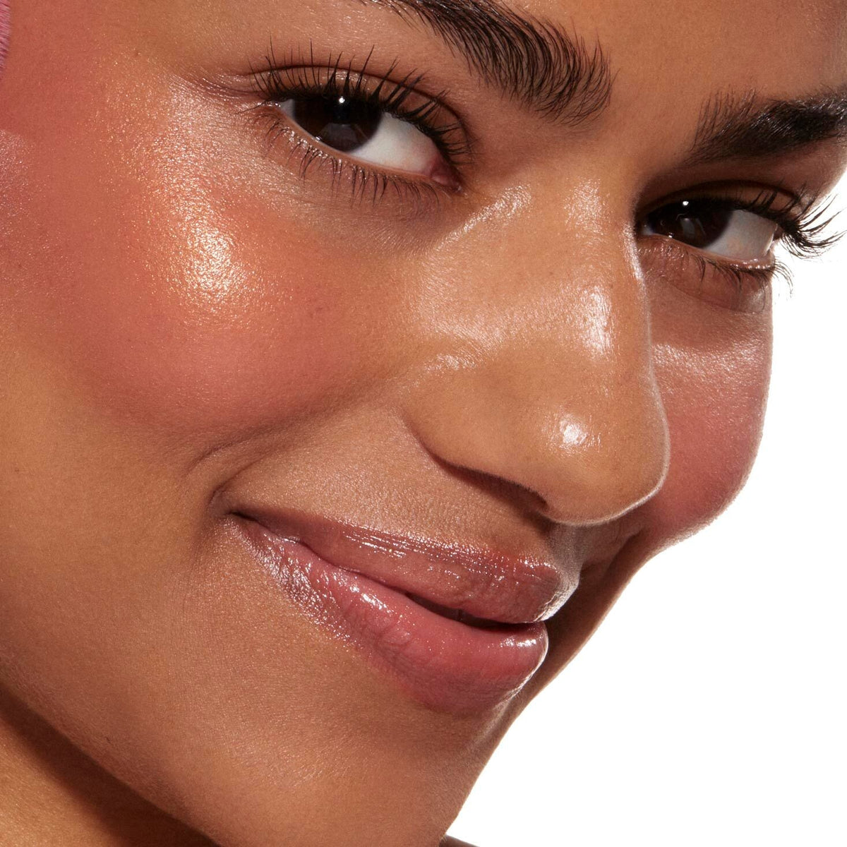Close-up cheek and lips wearing Princess Ave ColourPop Liquid Blush, delivering a dewy peachy-pink flush with soft shimmer, shown on a smiling model with defined lashes and glossy nude lips against a white backdrop.