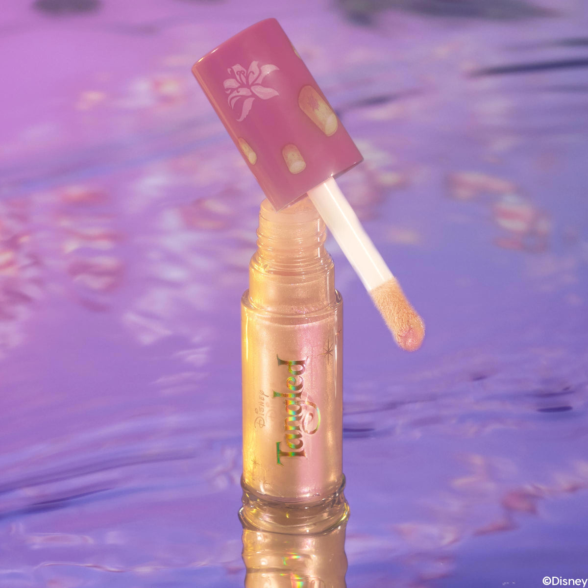 I See the Light ColourPop Liquid Highlighter stands upright with a doe-foot applicator lifted from the vial, revealing a pearlescent gold-pink sheen; lantern-patterned mauve cap and Tangled branding glow against a reflective purple water backdrop.