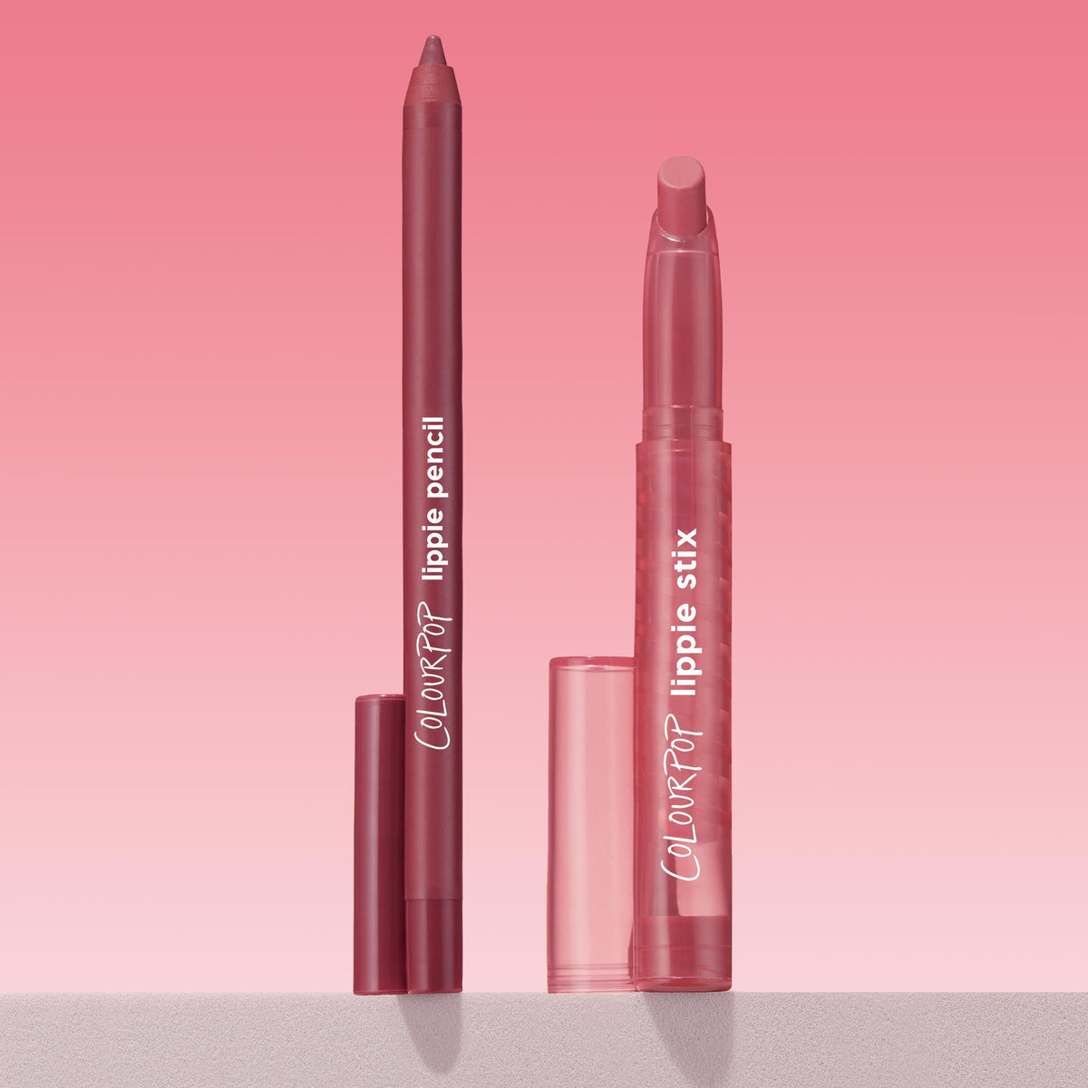 ColourPop Lippie Pencil Shot Clock stands uncapped beside matching Lippie Stix, both in rosy mauve, upright on a light surface against a pink gradient backdrop, highlighting the precise liner tip and branded tubes.