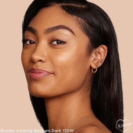 Model showcasing Medium Dark 120W shade, wearing ColourPop Pretty Fresh Creamy Concealer for a smooth, radiant natural finish; close-up side profile with glossy lips and small gold hoop earring against a soft beige background.