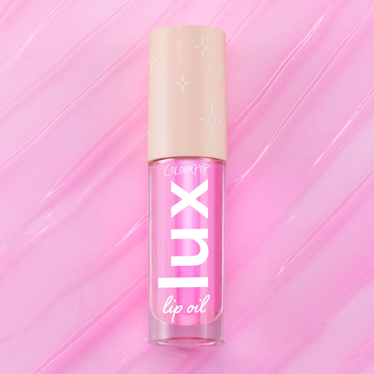 ColourPop Lux Lip Oil in Raspberry Mojito, a clear tube with bold “LUX” lettering and a beige star-print cap, displayed on a glossy swirled pink background, showcasing the vibrant pink-tinted lip oil formula.