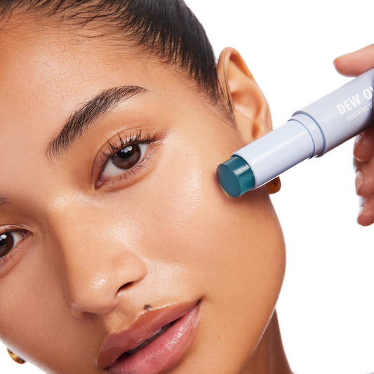 Dew Over Serum Stick glides across a model’s cheek, its teal hydrating core in a pale blue twist-up tube delivering a dewy glow on clean skin; ColourPop Serum Stick shown in use for quick, on-the-go skincare.