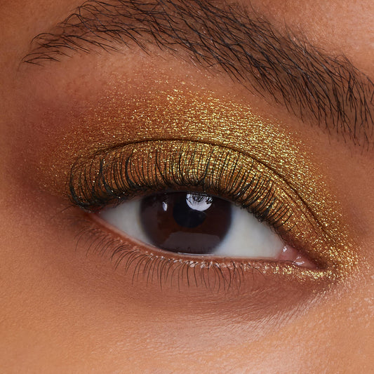 Open eyelid wears metallic gold shimmer, showcasing ColourPop Moonwalk Super Shock Shadow’s sparkling finish on smooth skin and defined lashes in a tight studio close-up.