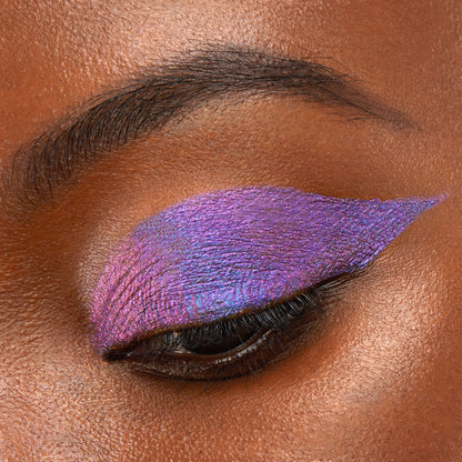 Same Vibe ColourPop Chrome Liquid Shadow swept across a closed eyelid in a sharp wing, showing a high-shine duochrome shift from violet to fuchsia with a blue‑teal sheen; smooth, opaque payoff in a close-up beauty swatch.