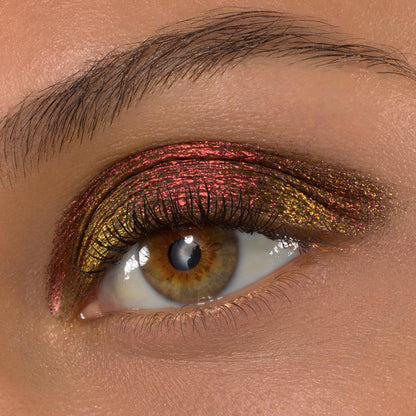 Vampire Girl ColourPop Shadow Stix sweeps across a hazel eye, creating a metallic multichrome look that shifts from ruby red to antique gold on the upper lid, framed by defined lashes and a natural brow in a macro beauty shot.