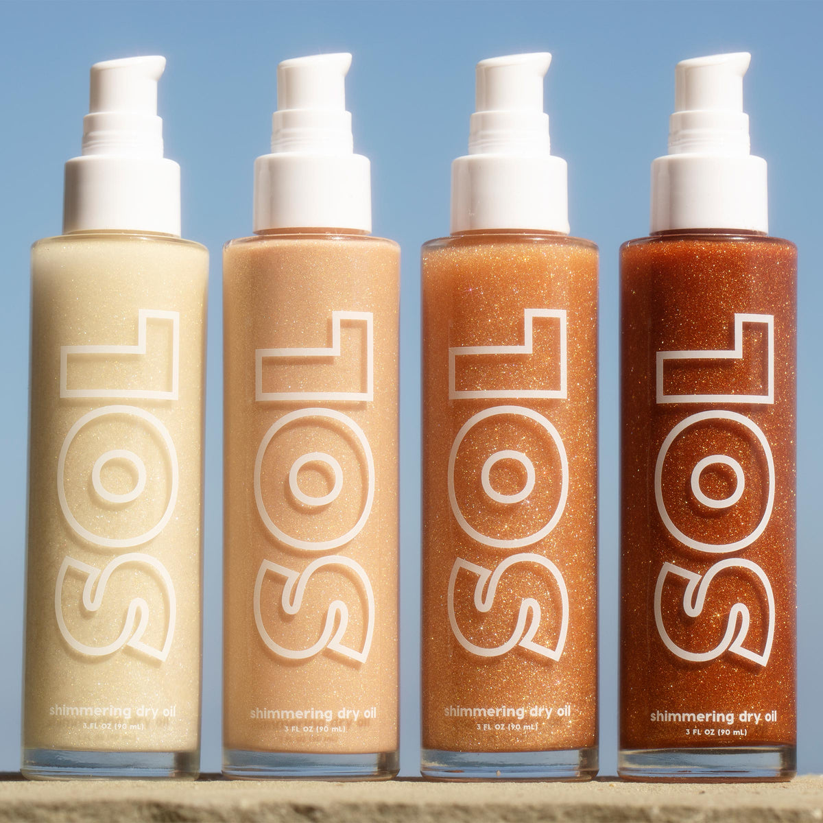 ColourPop SOL Shimmering Dry Oil in Warm Gold stands beside three deeper bronze shades, pumps up, sparkling in sunlight on a stone ledge against a blue sky; tall 3 fl oz bottles with bold SOL logo show golden shimmer.