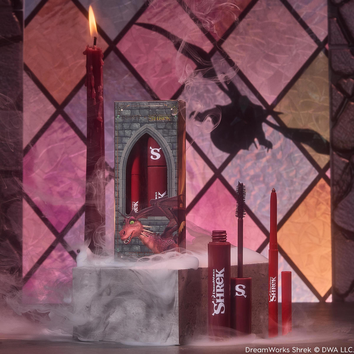 ColourPop Crème Gel Liner Dragon’s Keep displayed uncapped with fine tip beside matching tube and castle-themed Shrek box, in red packaging, with smoke on a stone pedestal, a lit red candle, and a stained-glass dragon shadow in the background.