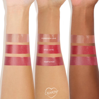 ColourPop So Juicy Plumping Gloss in Spice Level swatched in a bold, glossy stripe on three arms (light, medium, deep), shown between Forbidden Love and Temptation; rich cherry-red tint with a high-shine, plumping finish.