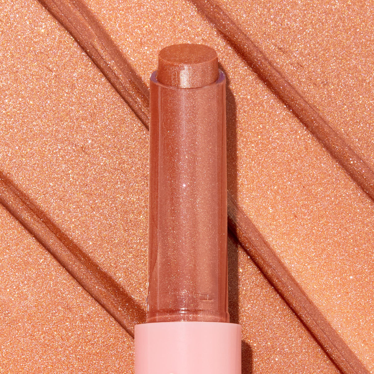 Angel Baby ColourPop So Juicy Plumping Gloss Balm with Peptides extends from a pink tube, the shimmery peach-nude bullet catching light, shown atop matching metallic swatches to highlight its glossy, plumping finish.