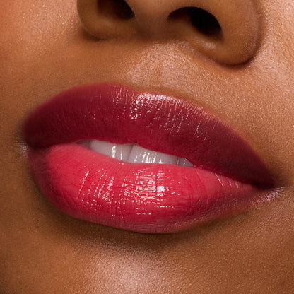 Glossy, plumped lips wearing ColourPop So Juicy Plumping Gloss in Spice Level, showing a sheer cherry-red shine with high reflection; macro close-up of a model’s mouth against smooth skin, highlighting hydration and a cushiony finish.